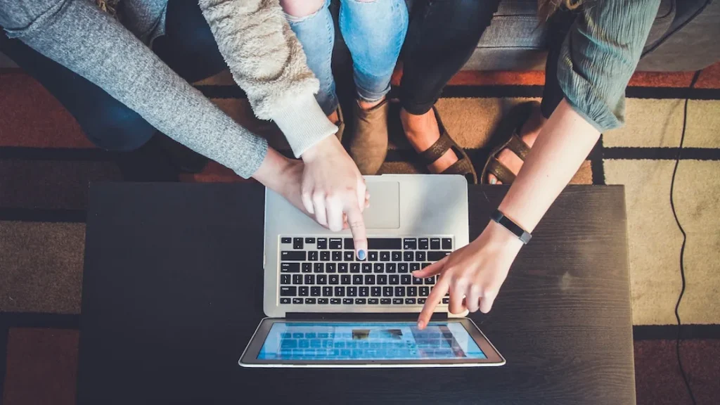 Três pessoas reunidas à volta de um portátil, apontando para o ecrã enquanto navegam online juntas.