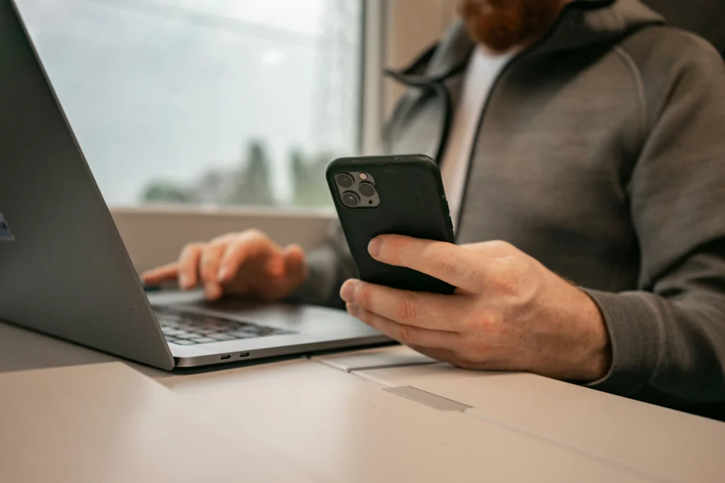 Um proprietário de salão gere as marcações online no telemóvel enquanto usa o portátil