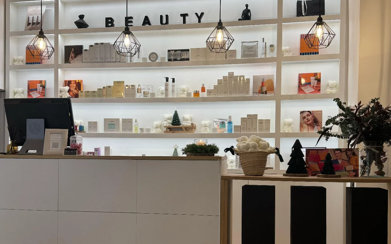 Uma receço luminosa e moderna com uma grande estante branca retroiluminada, cheia de vrios produtos de cuidados de pele. Candeeiros geométricos pendentes em arame preto pendem do teto, e o balco de receço é branco e minimalista.
