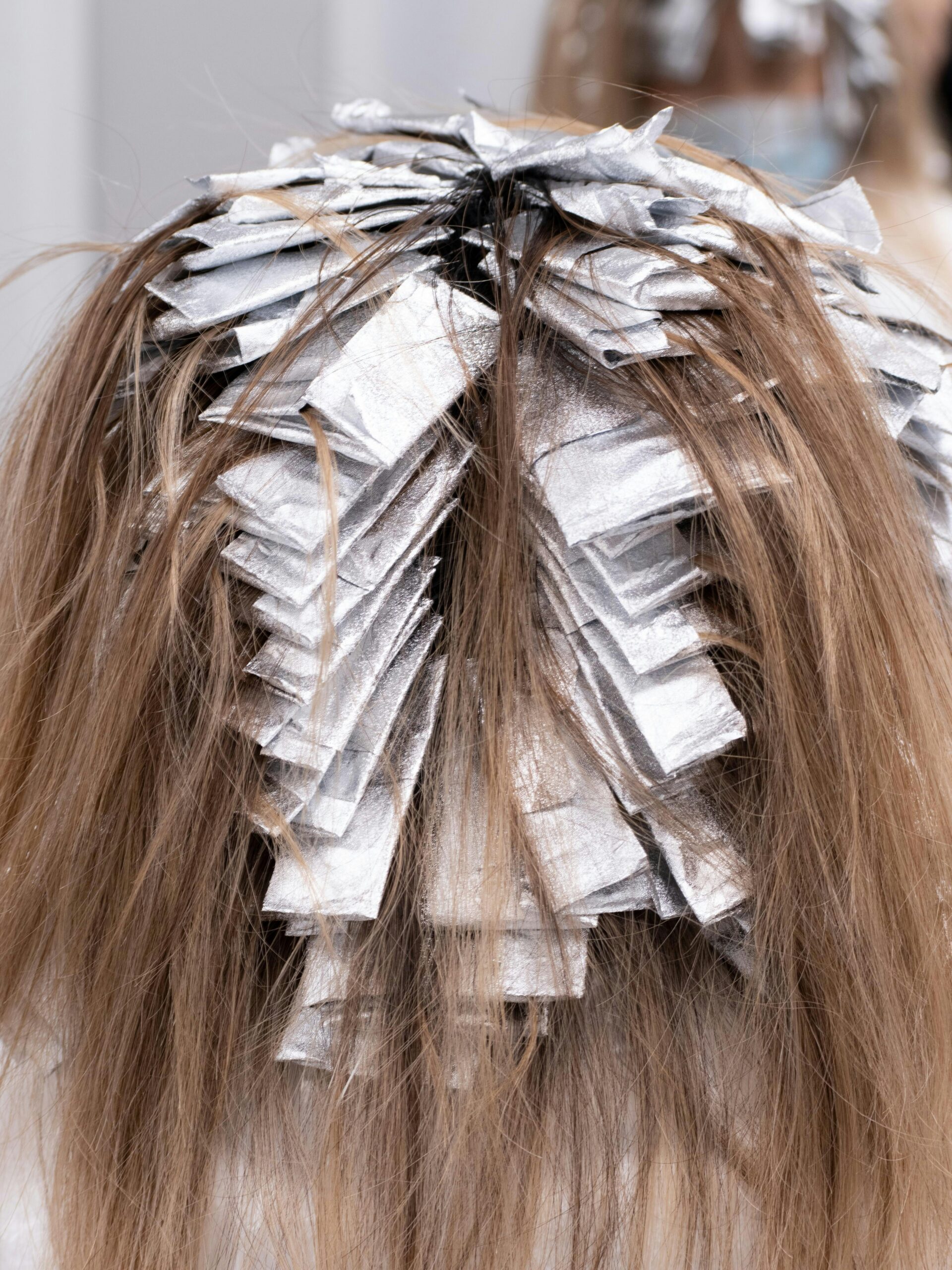 Parte de trás da cabeça de uma cliente com papel de alumínio no cabelo, a fazer um tratamento de cobertura parcial no cabeleireiro