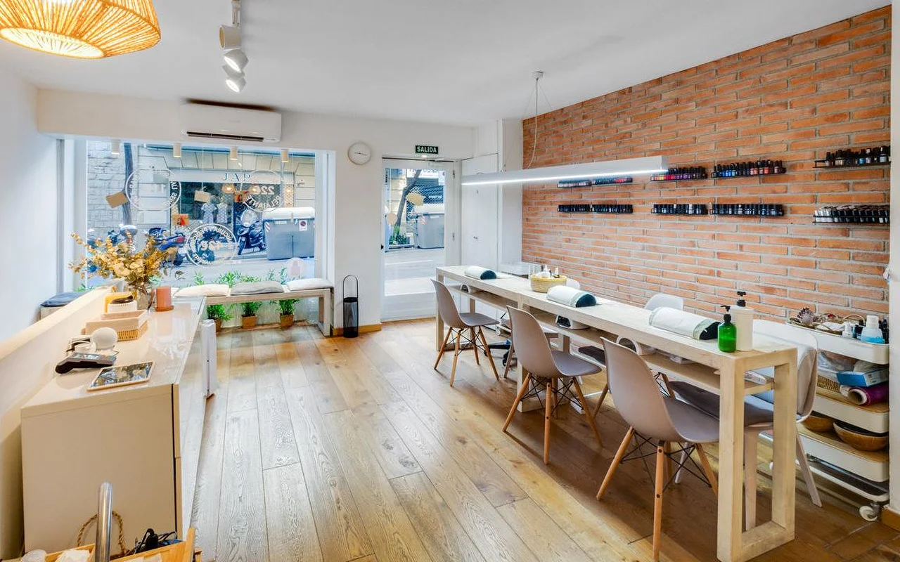 Um salo contemporneo com um toque rstico, apresentando um longo balco de manicure branco e uma parede de destaque em tijolo vermelho. Grandes janelas do para uma rua da cidade, inundando o espaço de cho em madeira com luz natural.