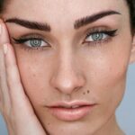 Close-up do rosto de uma mulher com microblading nas sobrancelhas, maquilhagem natural e cabelo escuro preso