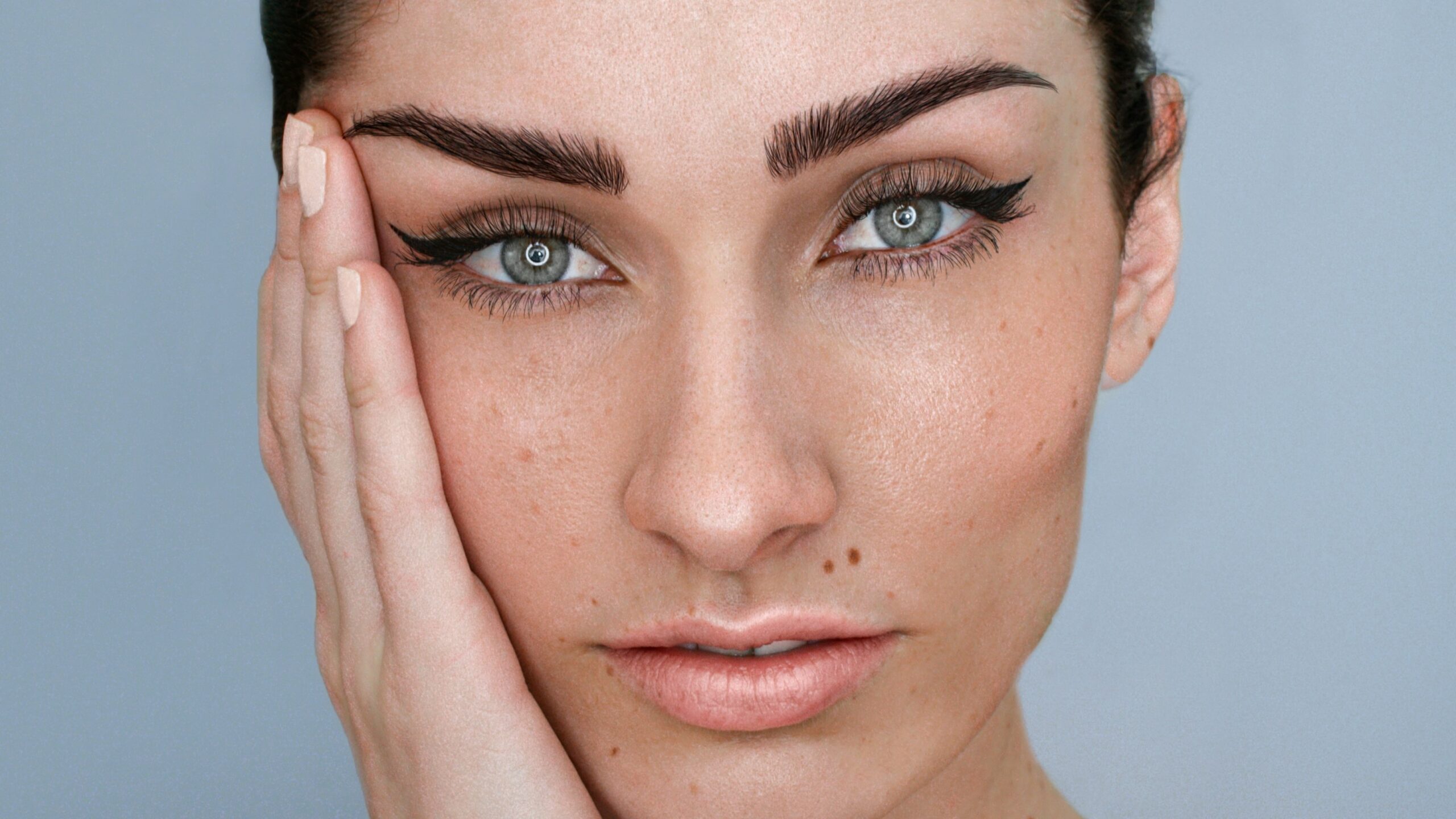 Close-up do rosto de uma mulher com microblading nas sobrancelhas, maquilhagem natural e cabelo escuro preso