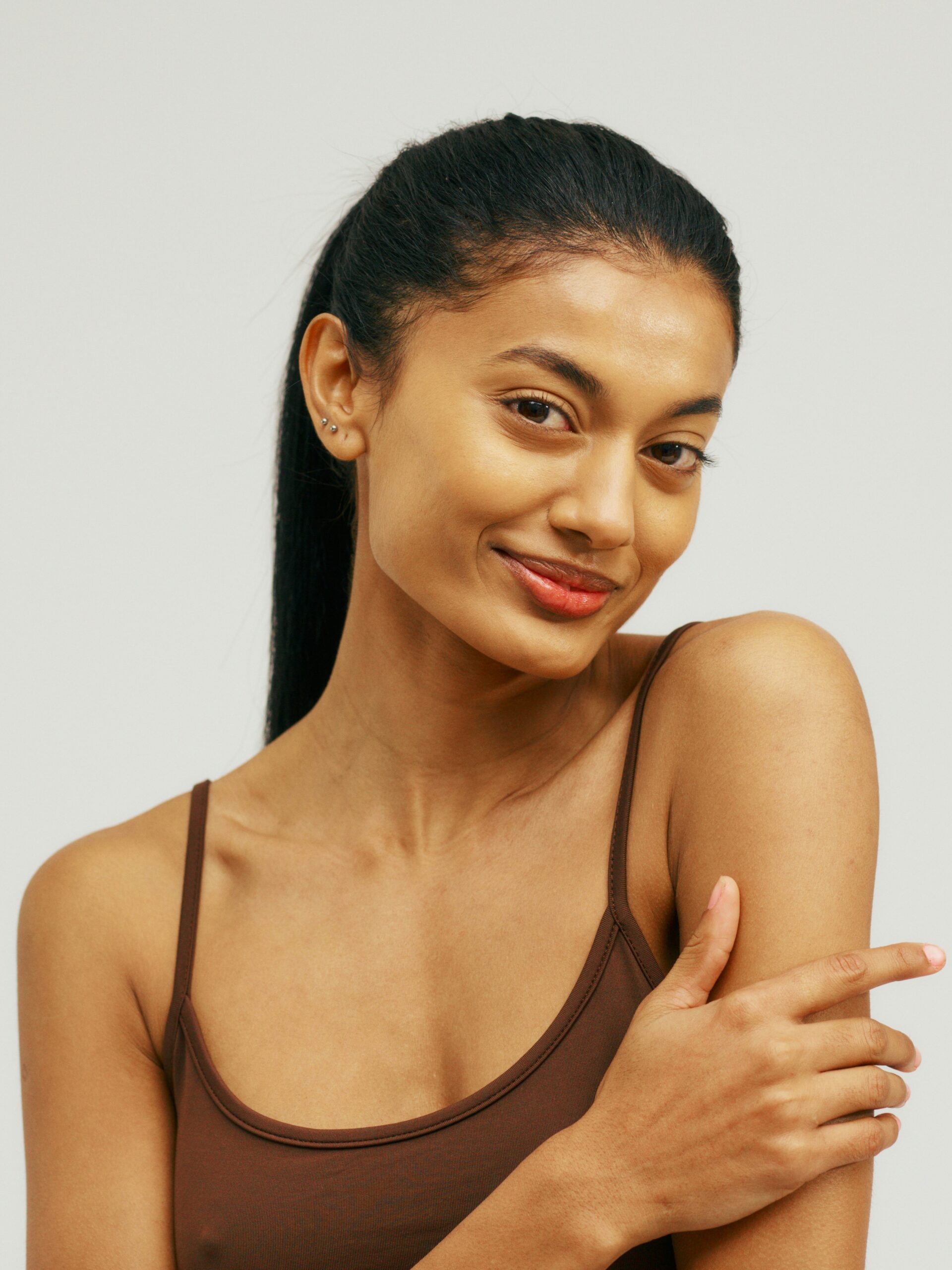 Retrato de uma jovem com uma camisola de alças a sorrir e a acariciar os braços lisos