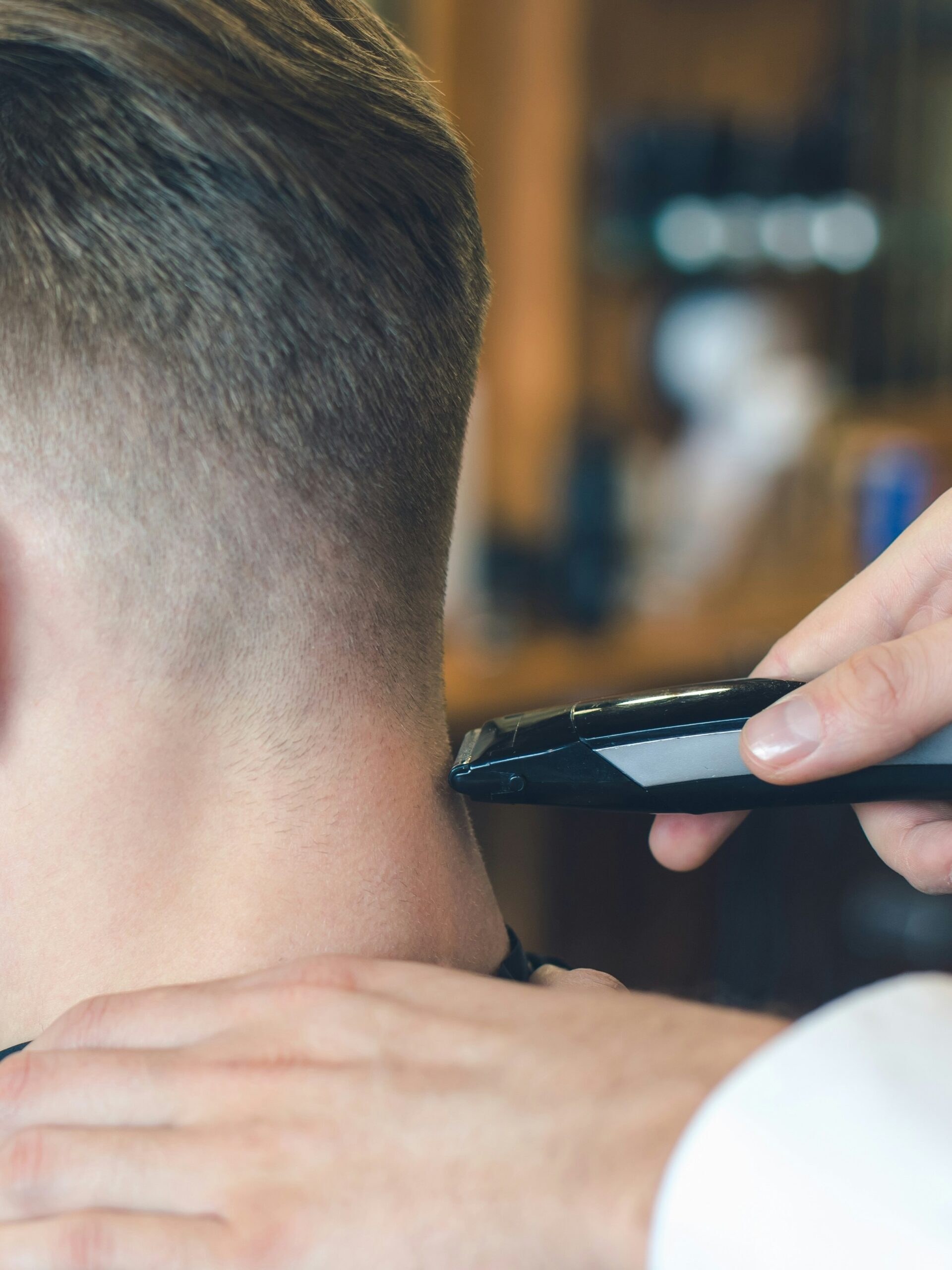 Close-up de um barbeiro a cortar um taper fade a um cliente com cabelo liso, usando a máquina na parte de trás da cabeça
