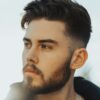 Homem de pé ao ar livre com cabelo escuro a exibir um corte taper fade com topo texturizado