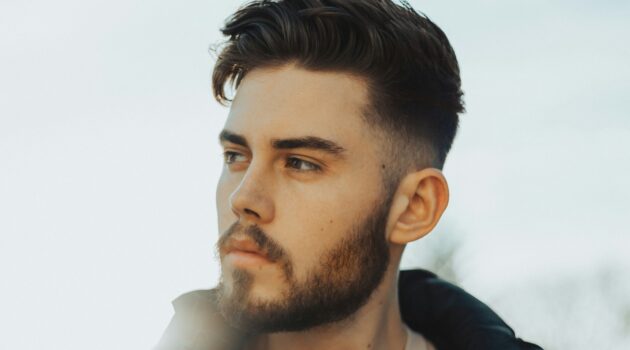 Homem de pé ao ar livre com cabelo escuro a exibir um corte taper fade com topo texturizado