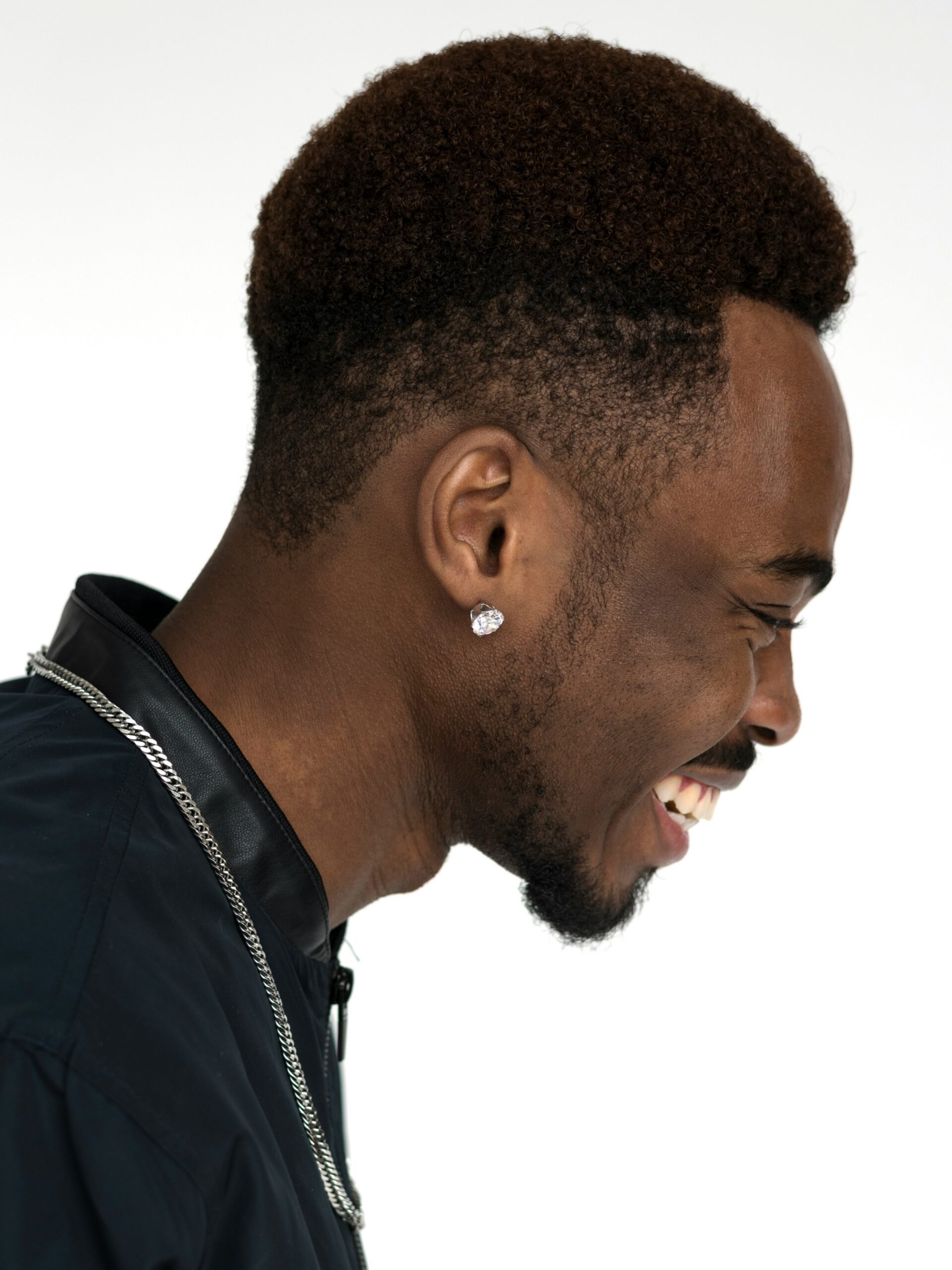 Perfil lateral de um homem a sorrir com cabelo afro combinado com um corte taper fade alto