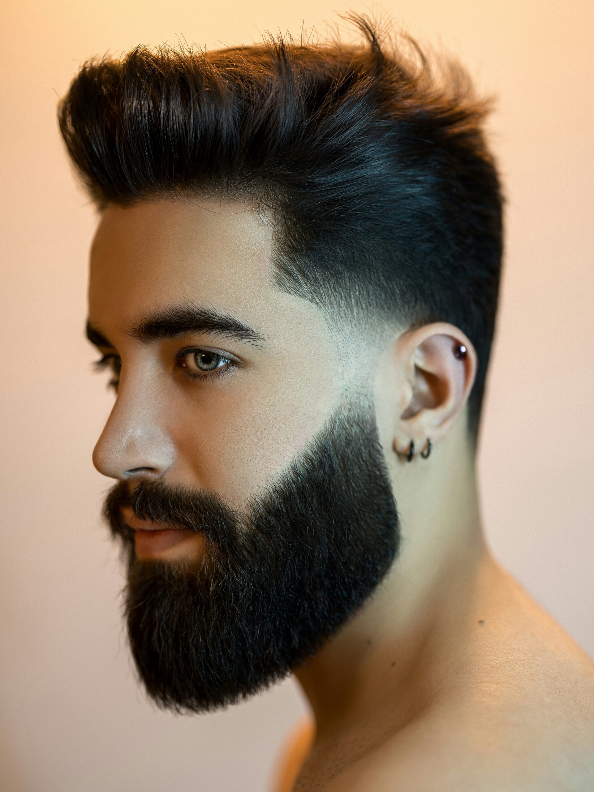 Homem com rosto oval e cabelo escuro a usar um taper fade baixo com volume e barba