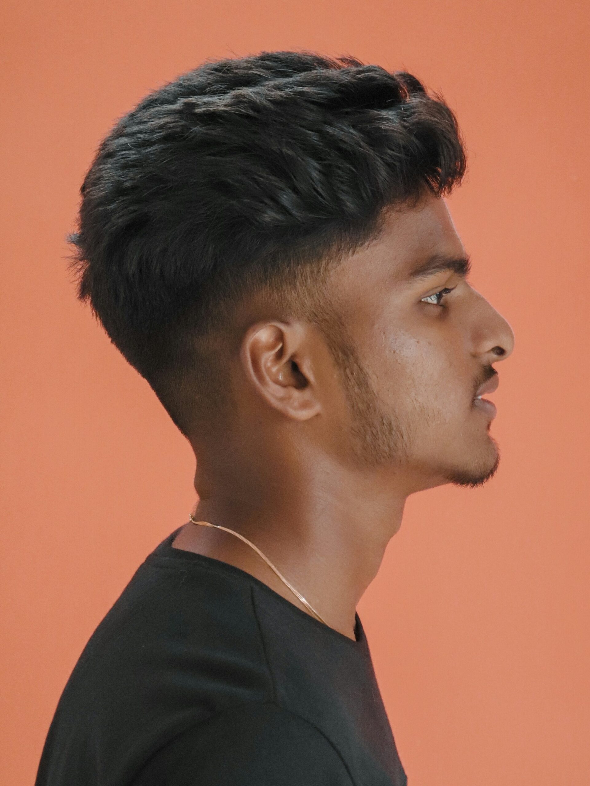 Retrato de perfil de um homem com penteado de volume texturizado combinado com um taper fade baixo