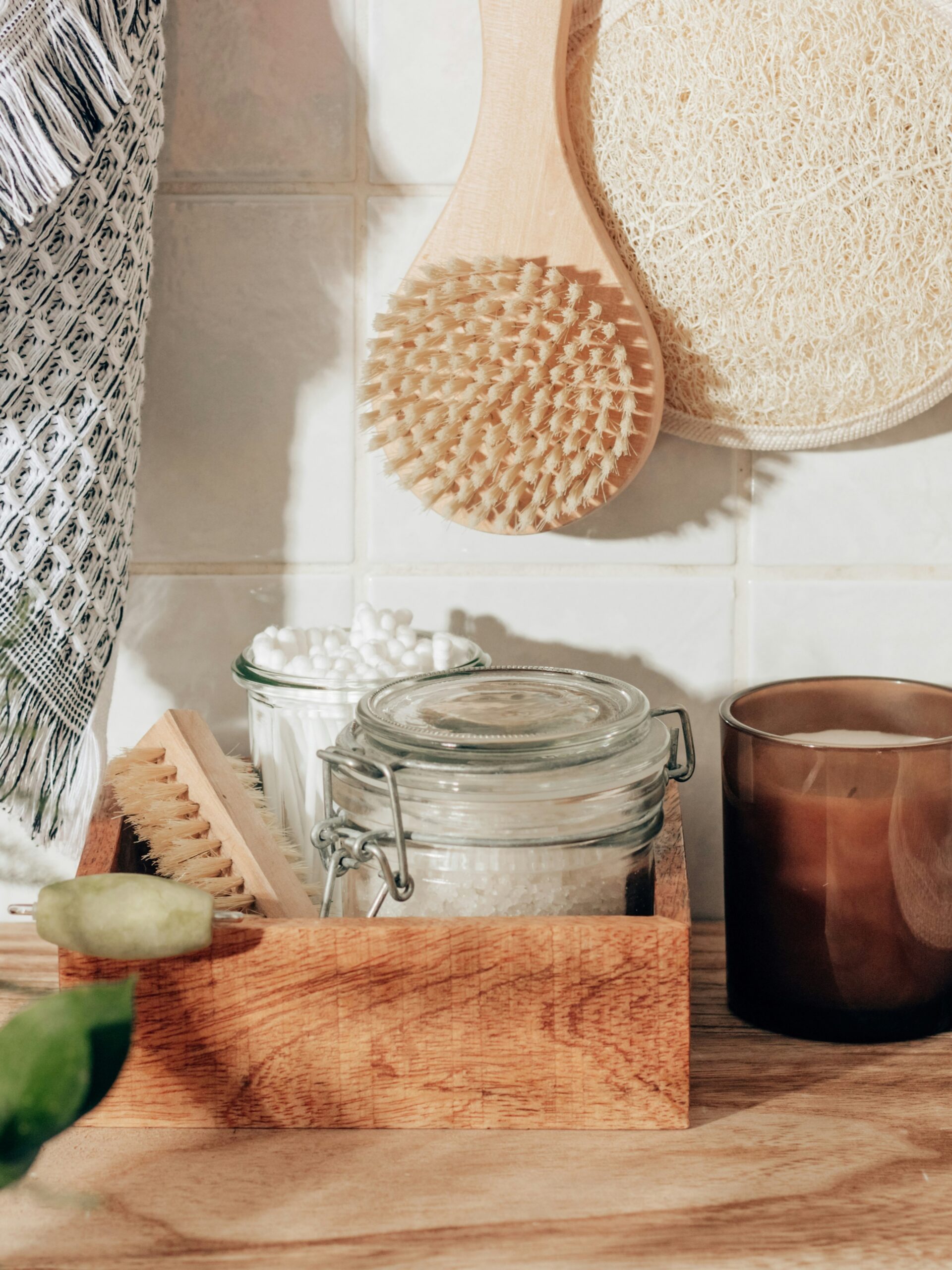 Composição de acessórios de casa de banho, incluindo luva esfoliante, escova corporal, sais de banho, cotonetes e uma vela