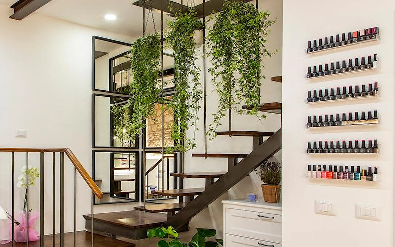 Um interior moderno e elegante com uma escada suspensa em madeira e metal. Plantas pendentes caem do teto entre os degraus, e filas de vernizes coloridos estão expostos em prateleiras transparentes na parede branca.