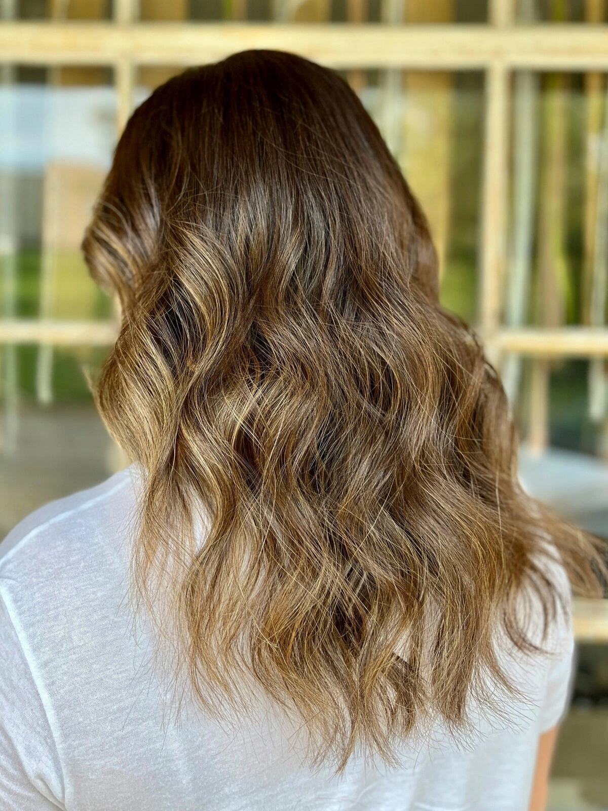 Vista de trás da cabeça de uma mulher com cabelo ondulado com balayage, em que a cor escura se esbate em tons quentes