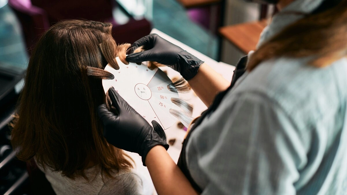 Grande plano de uma colorista que aproxima umas amostras de madeixas da cabeça de uma cliente para escolher os tons do balayage