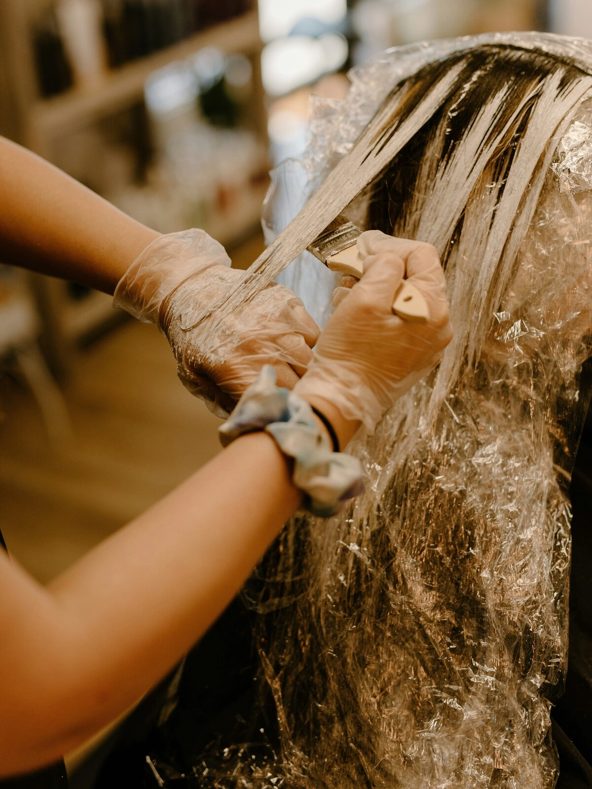 Uma colorista com luvas aplica a cor com um pincel sobre o cabelo de uma cliente, durante um balayage