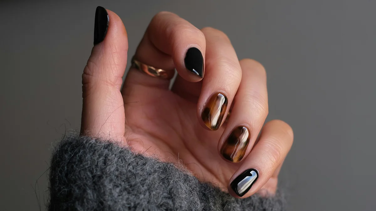 Grande plano de uma mão com unhas curtas e uma manicure em gel brilhante, em tons de preto e padrão animal
