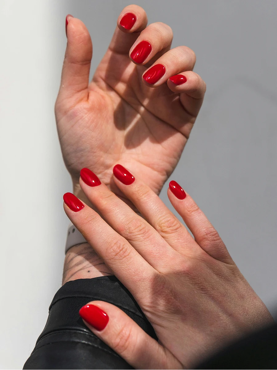Grande plano dos antebraços de uma mulher, com um casaco de cabedal preto e uma manicure em gel vermelho brilhante
