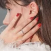 Vista lateral em grande plano da cabeça de uma mulher morena, com a mão a tocar no rosto e a exibir uma manicure em gel vermelho brilhante
