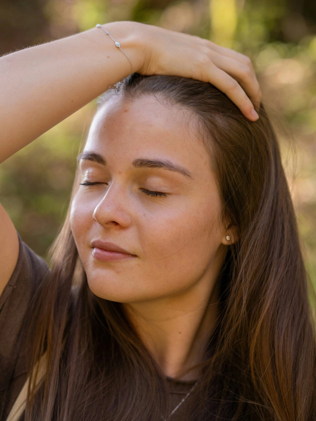 Uma mulher de olhos fechados e expressão relaxada passa a mão pela cabeça e pelo seu cabelo castanho comprido