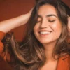 Grande plano de uma mulher a sorrir de olhos fechados enquanto passa as mãos pelo seu cabelo castanho, comprido e macio