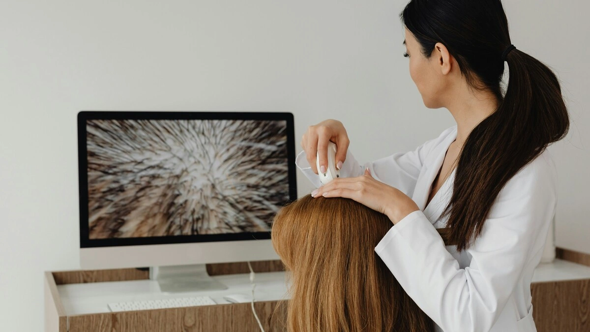 Um terapeuta a observar o couro cabeludo de uma cliente com uma câmara de alta resolução e a mostrar a imagem num ecrã grande