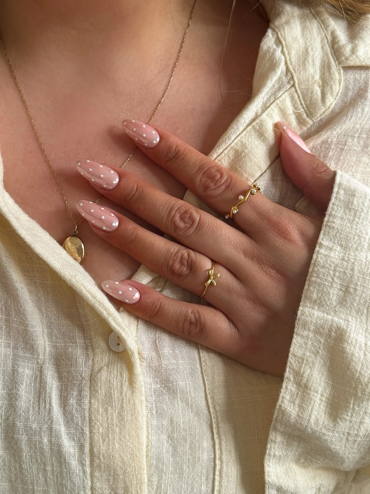 Unhas em formato amêndoa sobre base rosa transparente, salpicadas de micro bolinhas brancas distribuídas de forma uniforme.