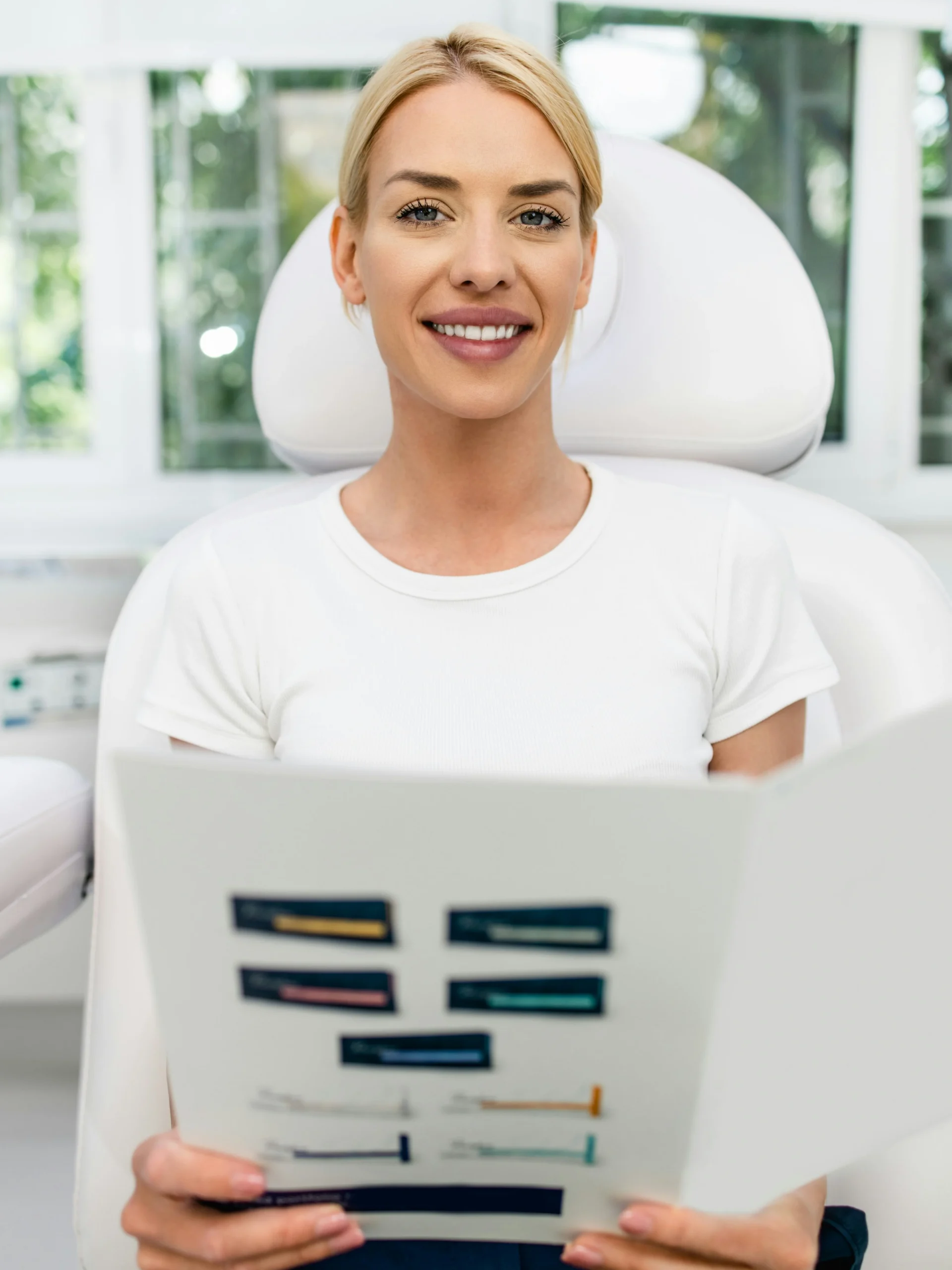Uma cliente sentada numa clínica luminosa e limpa, a sorrir enquanto segura um folheto informativo sobre tratamentos faciais