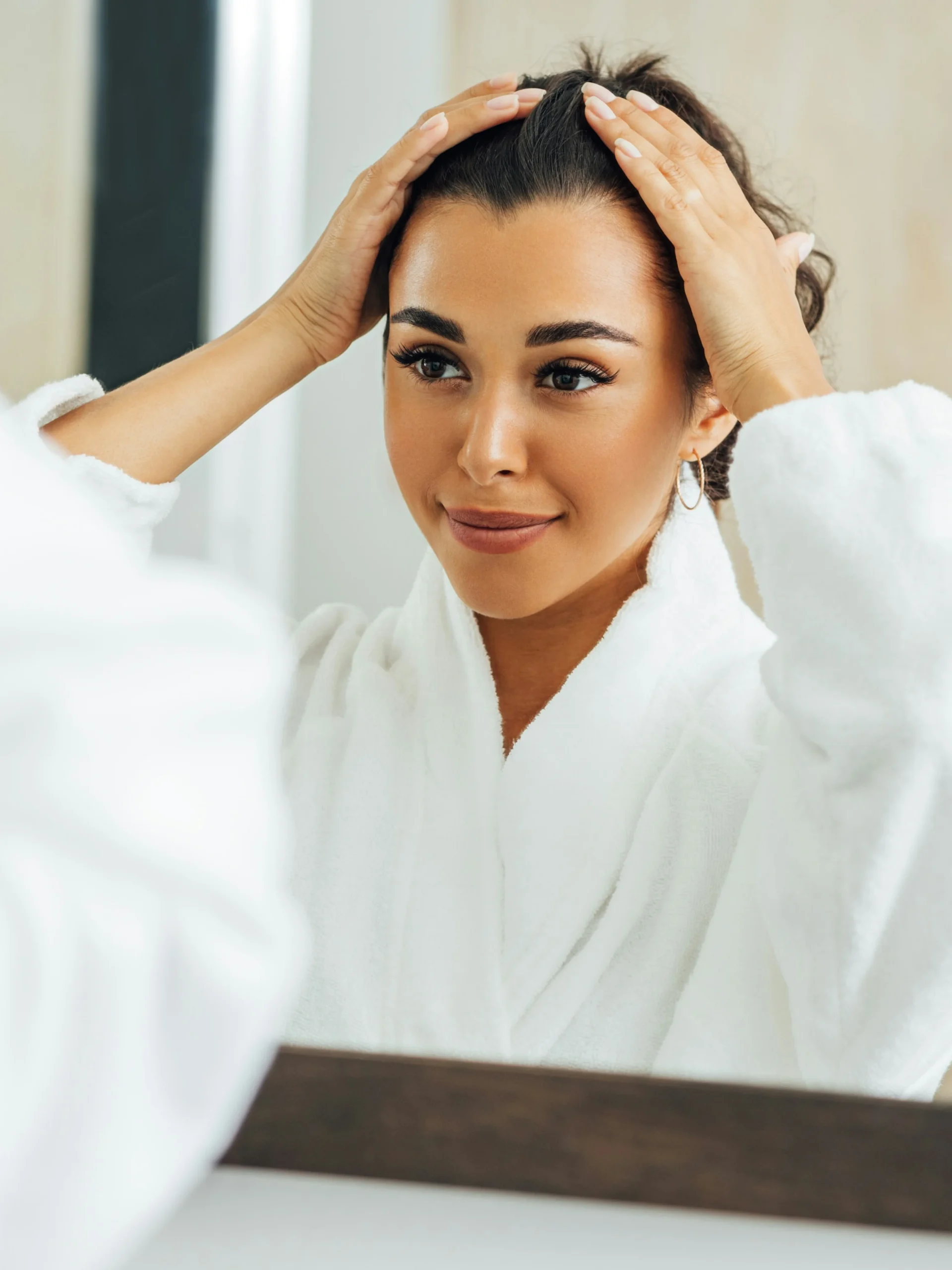 Mulher a afastar o cabelo do rosto e a sorrir enquanto se olha ao espelho