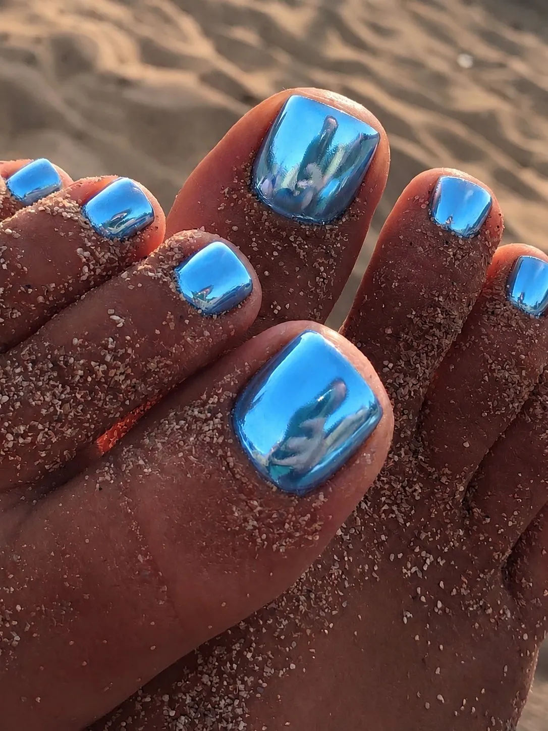 Pedicure cromada azul oceano metalizada em pés sobre a areia, na praia