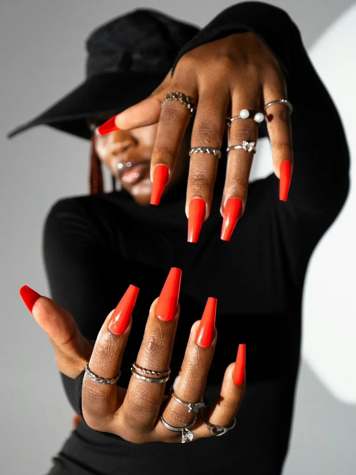 Uma mulher mostra as mãos com manicure à câmara, exibindo unhas de acrílico cor de laranja vivo em formato coffin