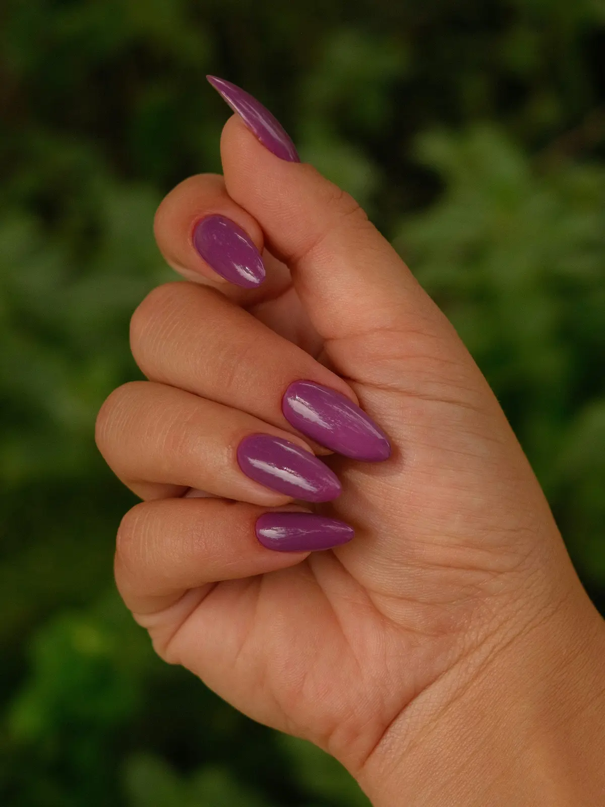 Grande plano da mão de uma mulher com unhas de acrílico roxas em formato amêndoa