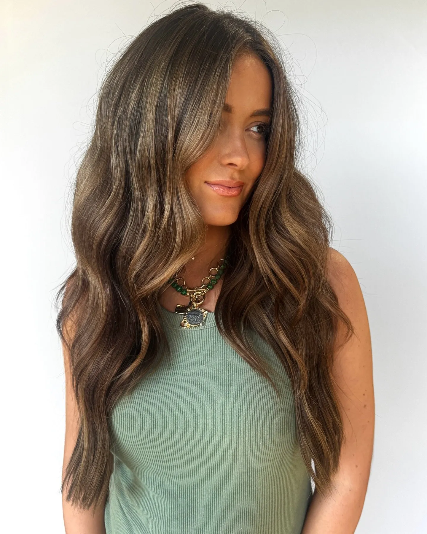 Cabelo comprido e castanho com ondas suaves e madeixas à francesa subtis, concentradas nas pontas