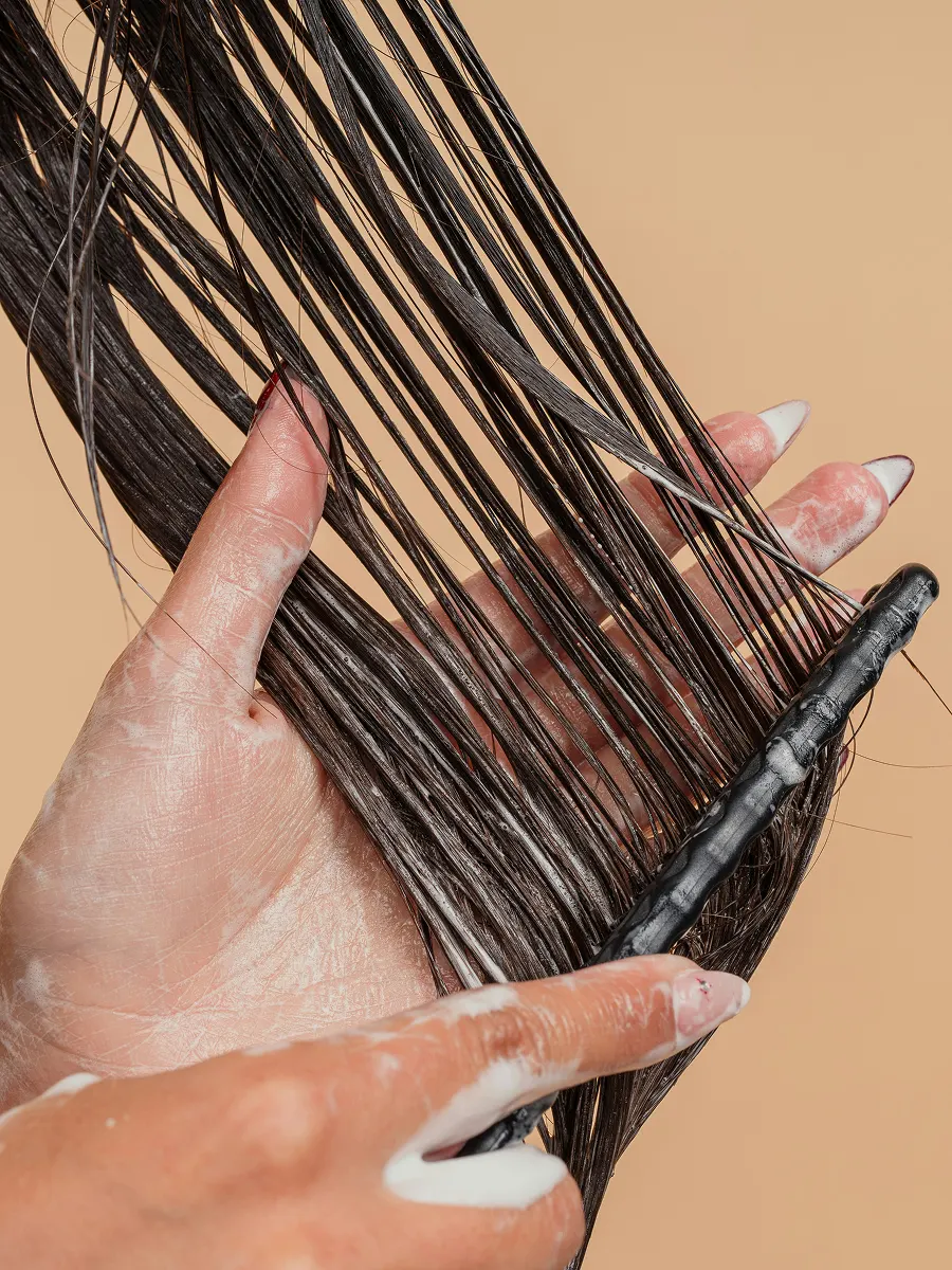 Grande plano de uma mulher a distribuir amaciador pelo cabelo comprido com um pente de dentes largos