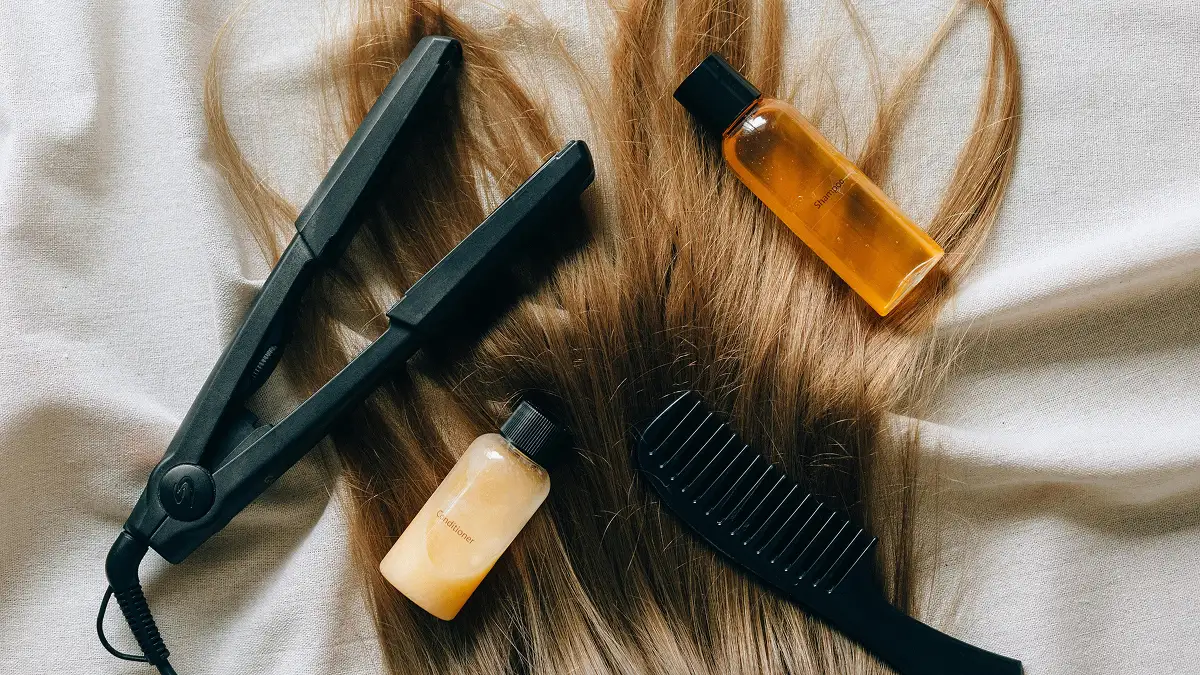Composição de produtos de cuidado capilar dispostos sobre o cabelo liso e comprido de alguém, incluindo champô, amaciador, prancha e um pente de dentes largos