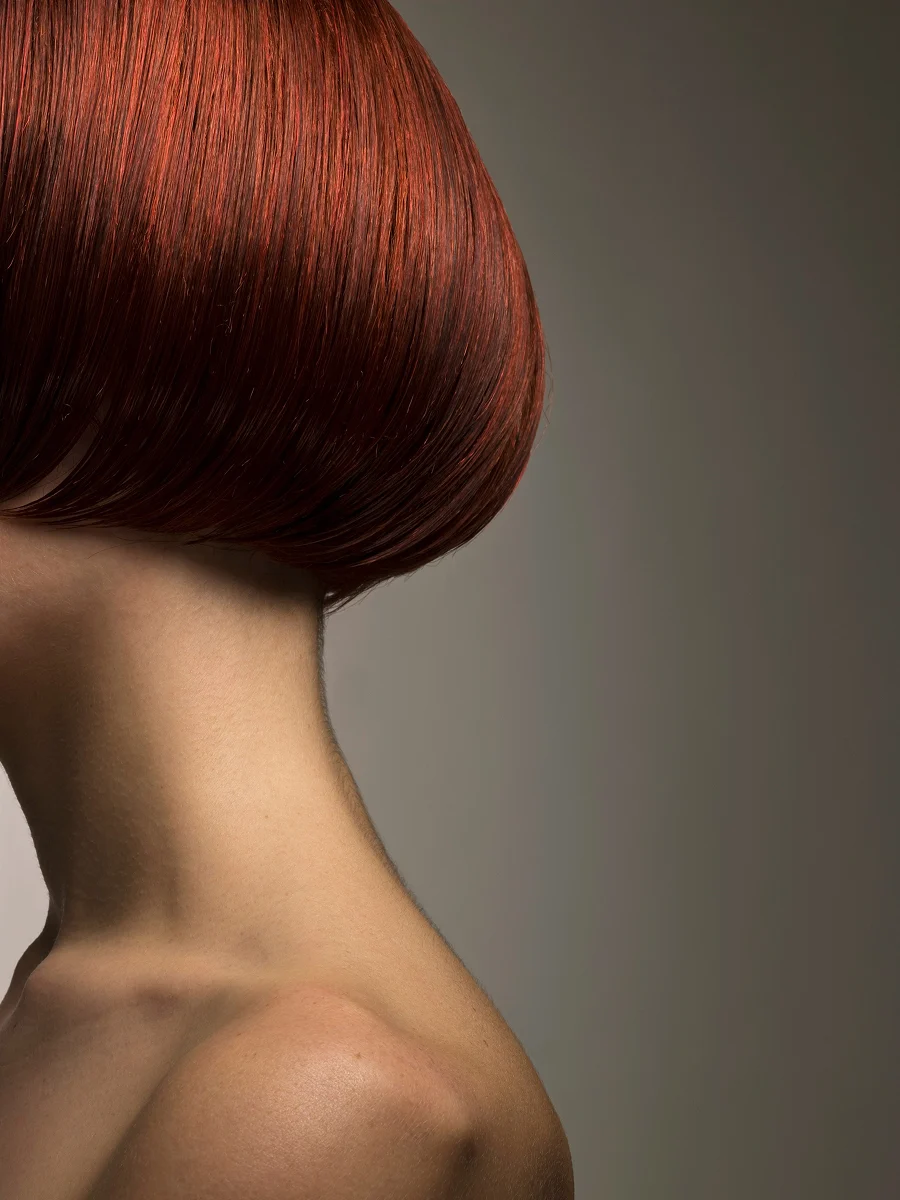 Grande plano, de perfil, da cabeça de uma mulher com um bob vermelho, pintado e brilhante