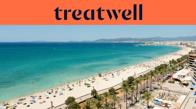 Vista aérea da Playa de Palma, em Maiorca, com uma longa curva de areia dourada, filas de chapéus de sol, água turquesa e calma e uma avenida marginal ladeada de palmeiras junto à cidade, com colinas ao fundo sob um céu azul e limpo.
