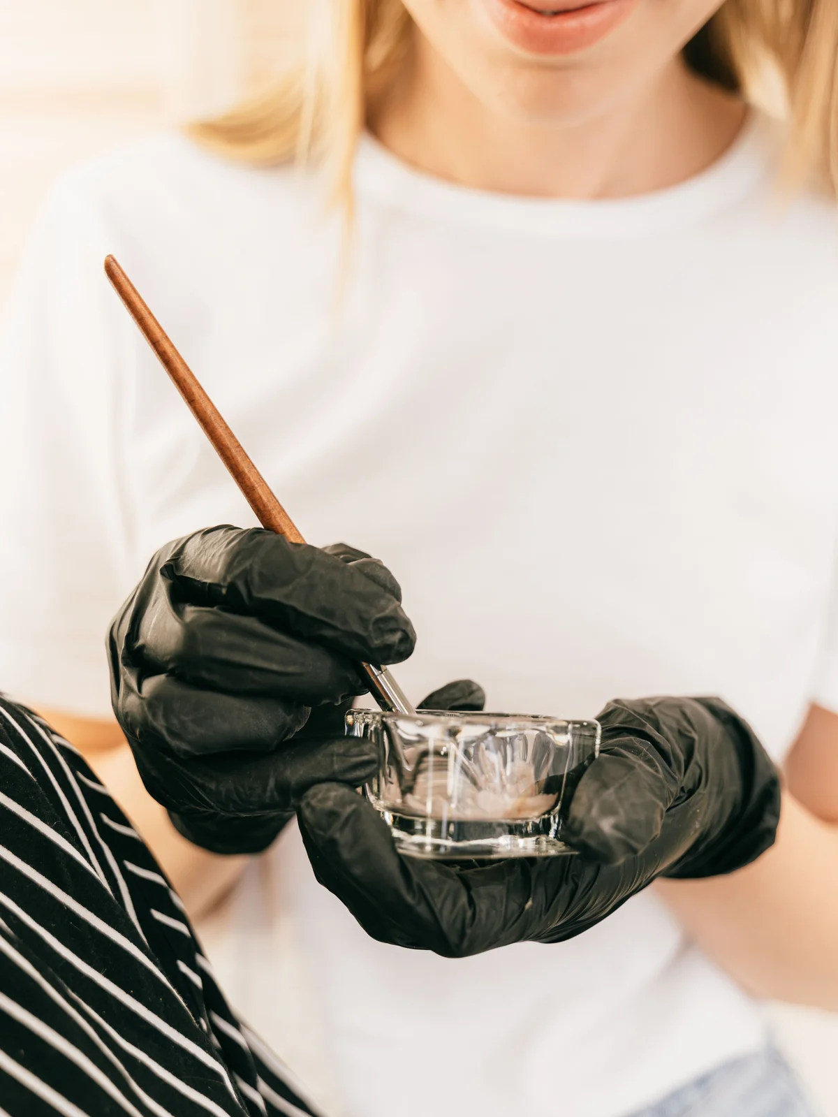Grande plano de uma esteticista a segurar um pequeno frasco de vidro e um pincel fino enquanto mistura a coloração de sobrancelhas no salão