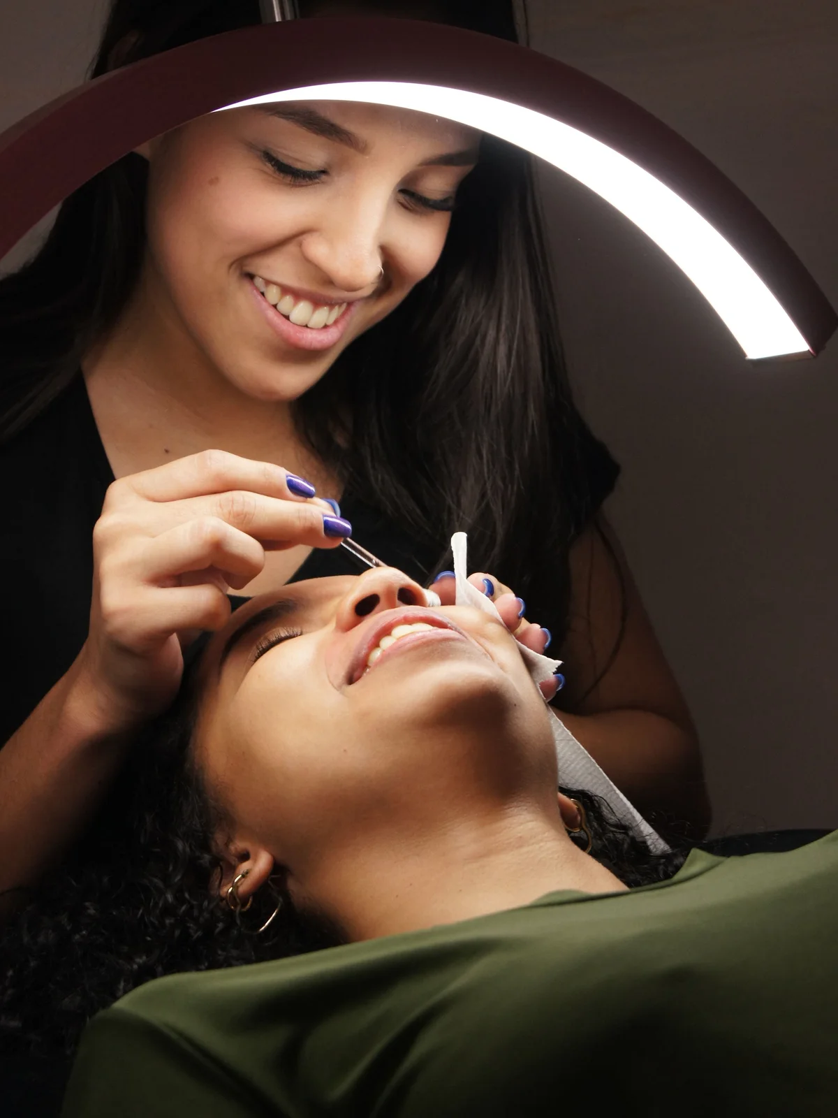 Grande plano de uma esteticista a aplicar coloração nas sobrancelhas de uma cliente que descansa relaxada na marquesa do salão
