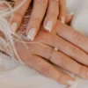 Manicure francesa clássica em branco sobre unhas naturais de formato quadrado, sobre um tecido branco