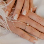 Manicure francesa clássica em branco sobre unhas naturais de formato quadrado, sobre um tecido branco