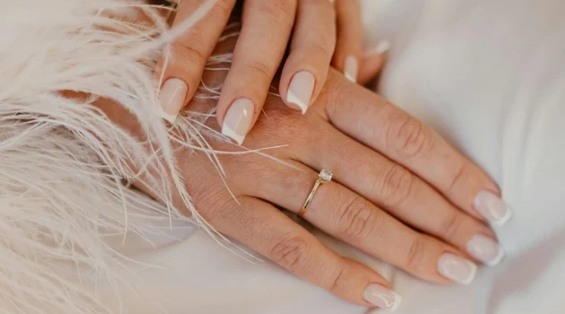 Manicure francesa clássica em branco sobre unhas naturais de formato quadrado, sobre um tecido branco