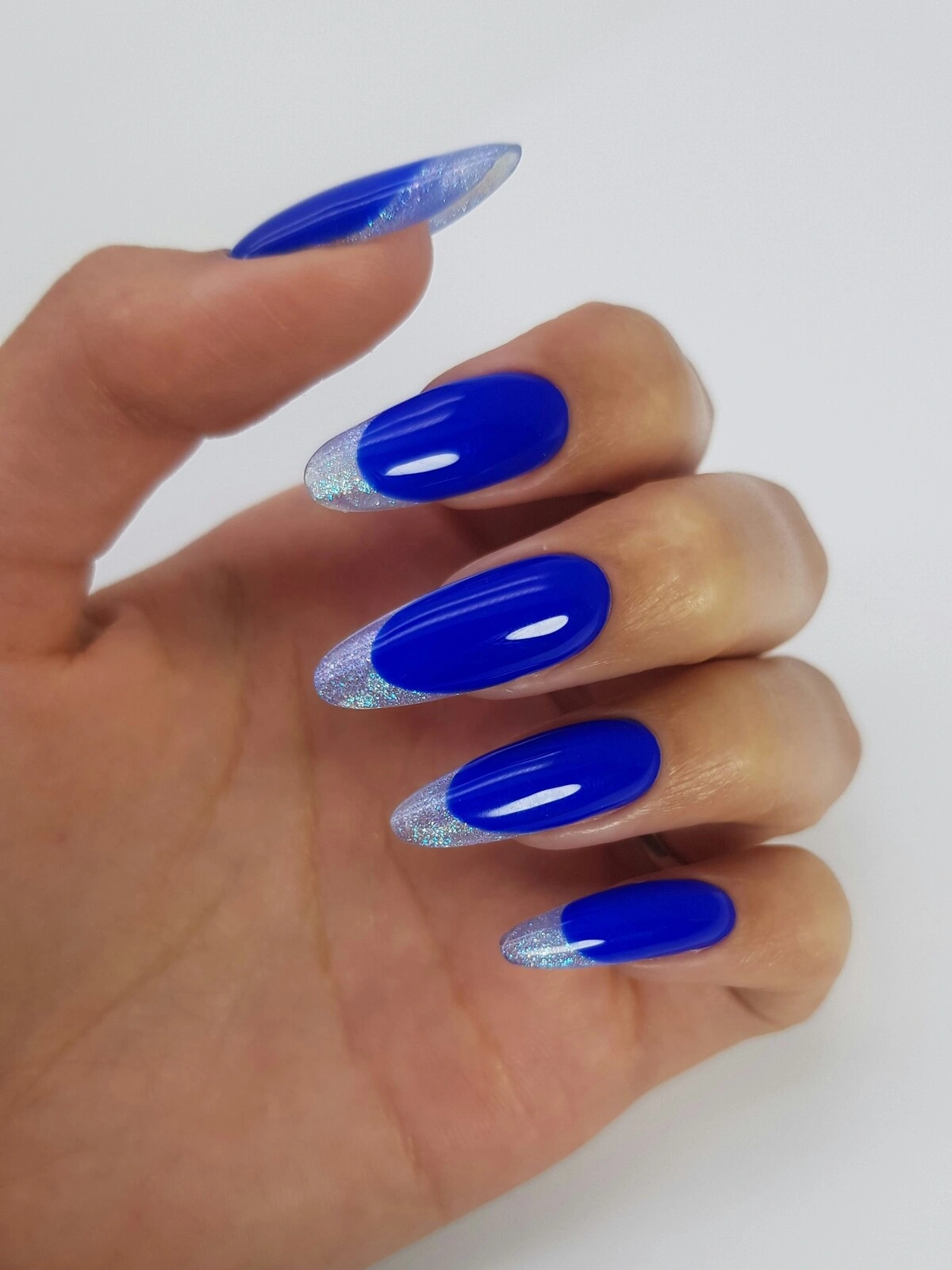A mão de uma mulher com uma manicure francesa ousada de base azul intenso e pontas metalizadas prateadas em unhas compridas amendoadas