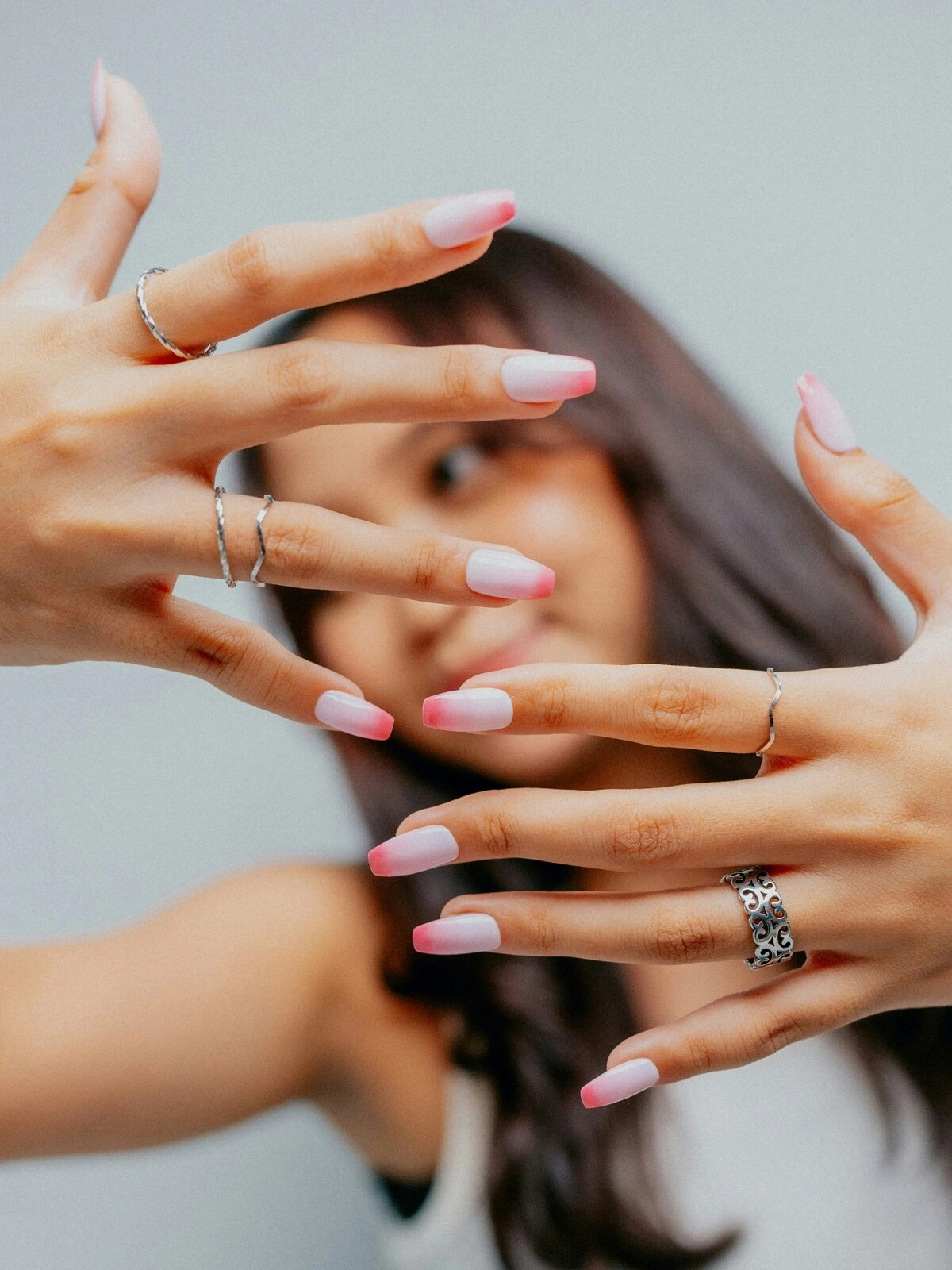 Uma mulher mostra as mãos à câmara com uma manicure francesa em versão ombré, de base rosa-claro e pontas cor-de-rosa vivo em unhas bailarina