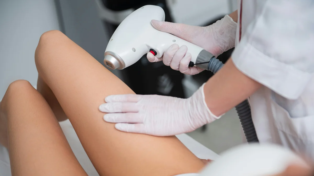 Grande plano de uma esteticista a tratar a parte inferior da perna de uma cliente durante uma sessão de depilação a laser