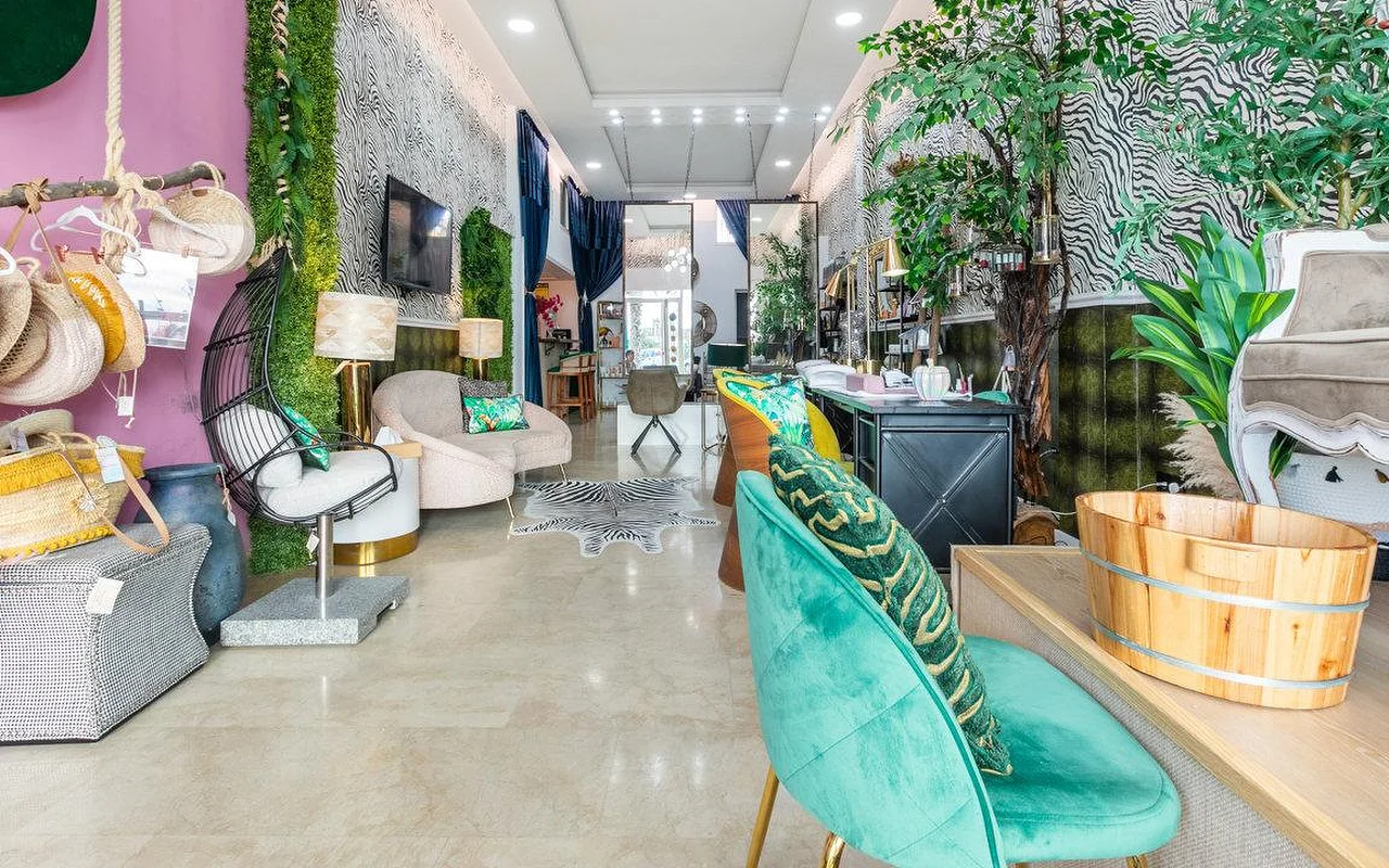 O interior da Brazilian Beauty Marbella, um salão luminoso com paredes de padrão de zebra, uma parede de plantas, cadeiras de veludo turquesa e um lava-pés de pedicure em madeira.
