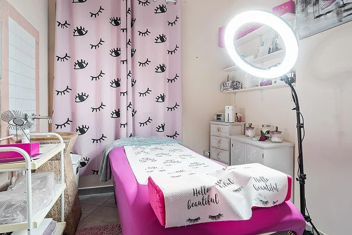 Sala rosa no Centro Estetico Karma em Olbia com cortinas com estampado de pestanas, marquesa e aro de luz.