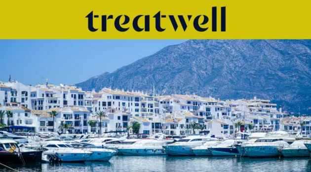 A marina de Puerto Banús, em Marbella, ladeada por edifícios brancos e iates atracados com as montanhas ao fundo, sob um banner amarelo da Treatwell.
