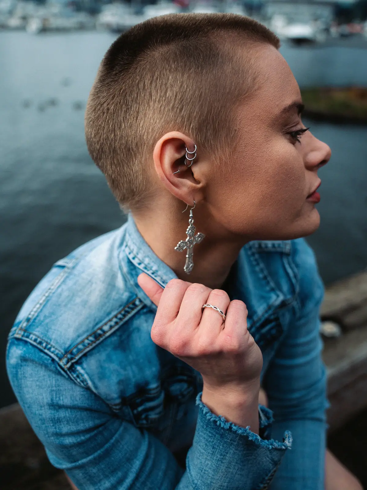 Fotografia de cima de uma mulher com furos no forward helix, na hélice e no lóbulo, sentada junto a um rio na cidade