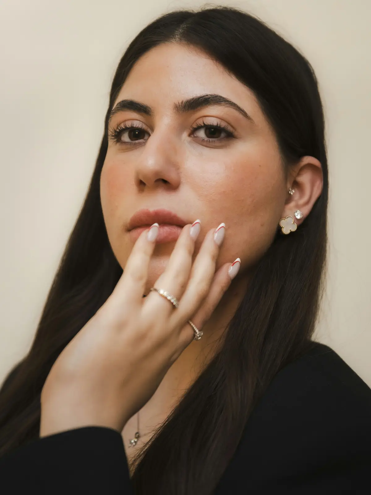 Fotografia de estúdio de uma mulher com furos no lóbulo e no tragus, com uma mão de manicure cuidada junto ao rosto