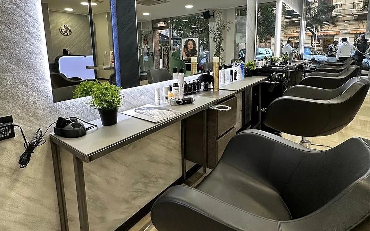 A zona de penteados da Equipe Beauty, com uma fila de cadeiras pretas ao longo de um balcão com efeito de mármore, um grande espelho retroiluminado, produtos de styling e uma planta em vaso sobre o balcão, e janelas do chão ao teto viradas para a rua.